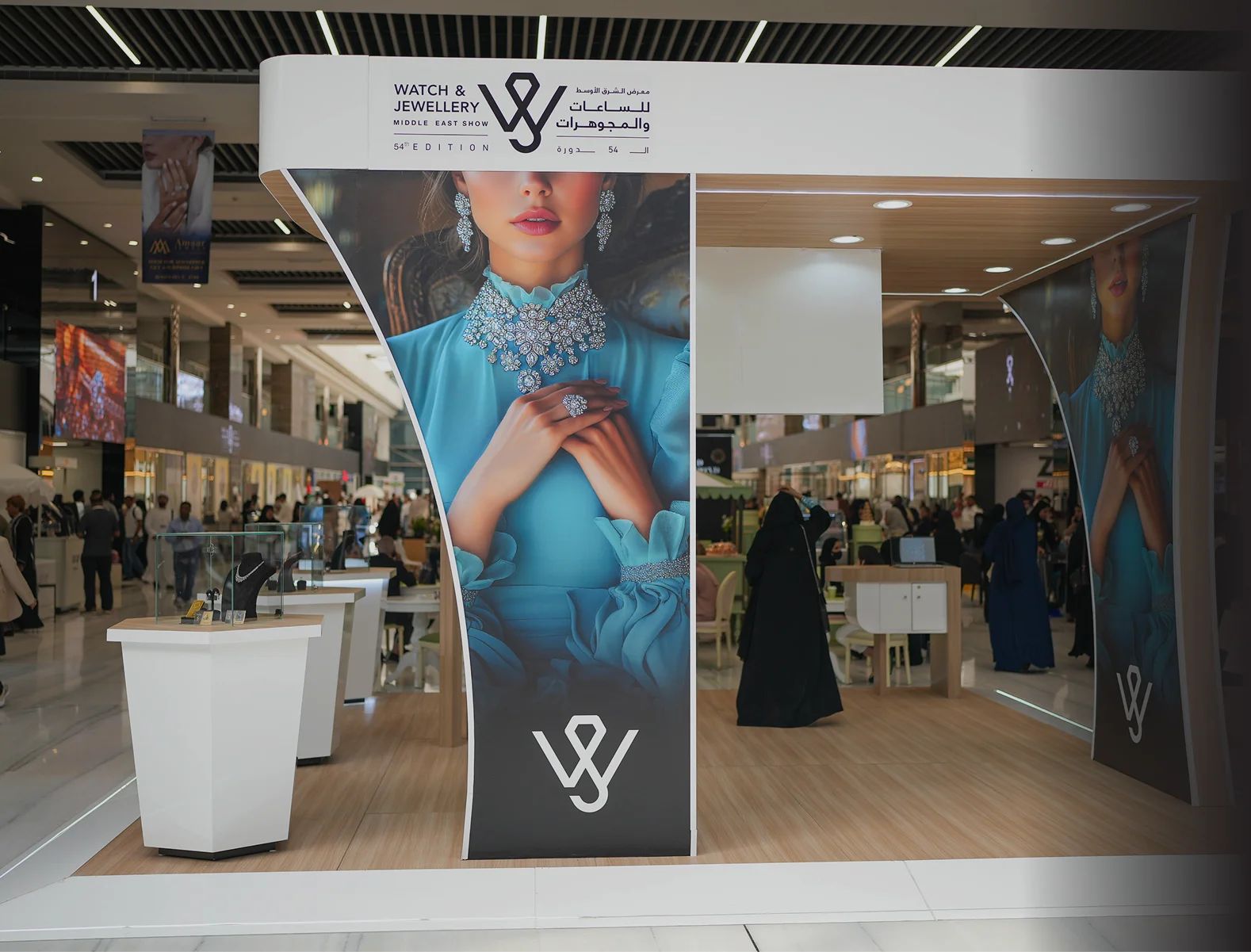 A woman stands in front of a large display showcasing watches and jewelry.
